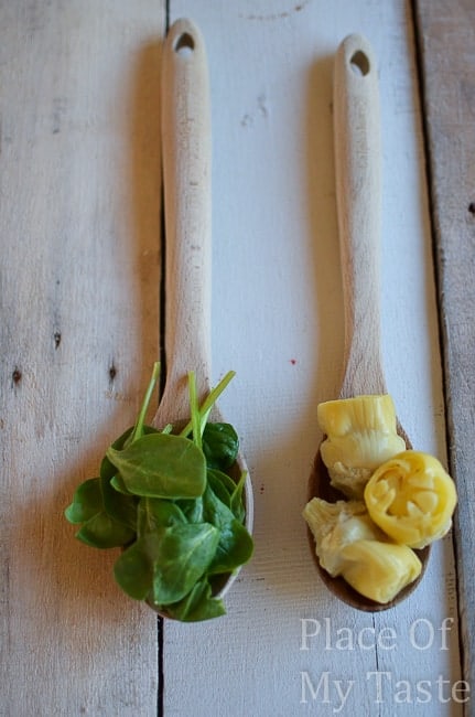 two spoons laying on a wooden background with spinach and artichoke