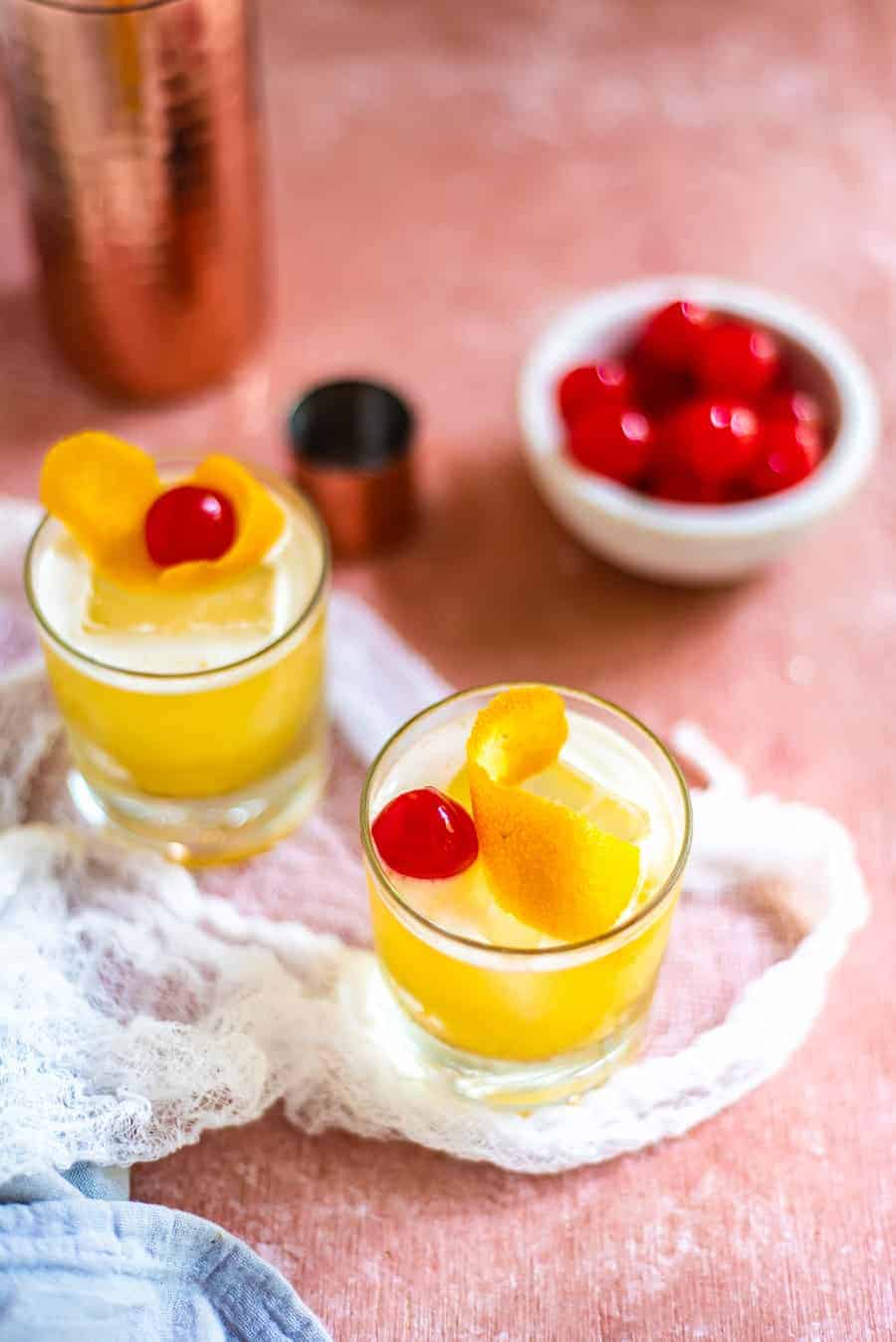 Whiskey sour in whiskey glasses embellished with cherries and orange peel 