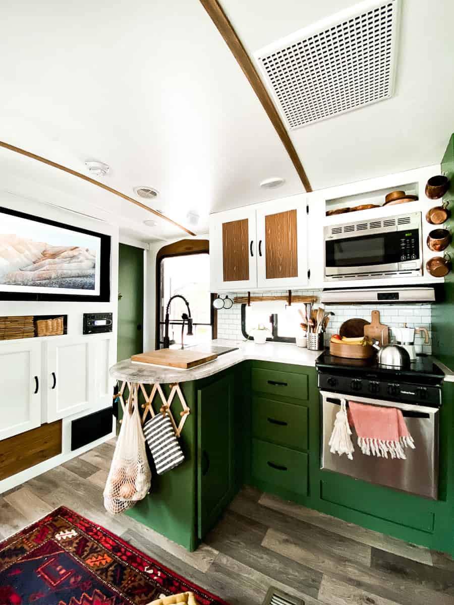 White and wood accents in a camper with green cabinets in a kitchen.