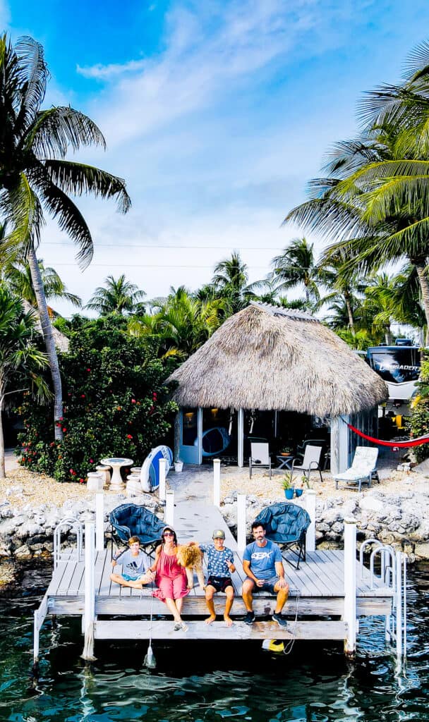 People sitting on a dock in the Florida Keys with a Tiki hut in the background.