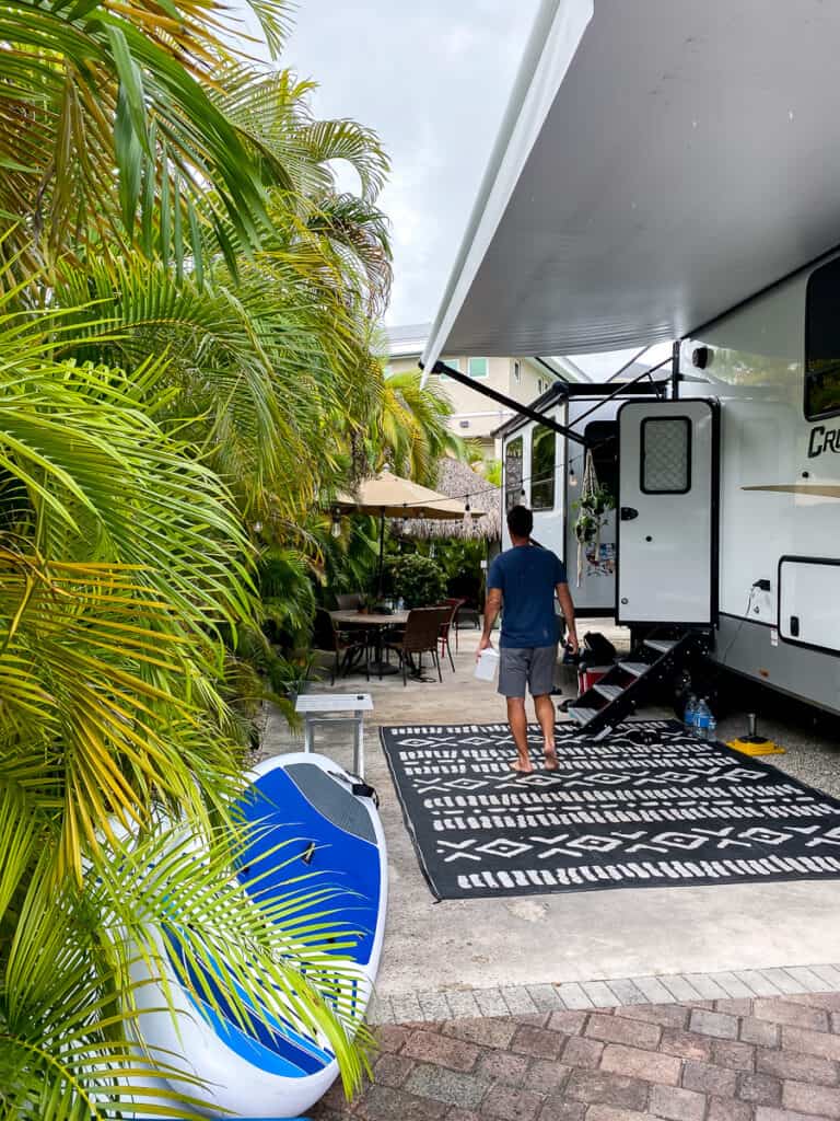 Palm trees and fifth wheel with a patterned camping mat.